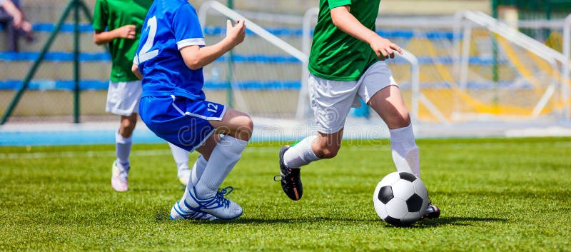 Children Soccer Players Running with the Ball. Kids in Blue and Green Soccer Jerseys Playing Football on the Pitch. Sports Stadium in the Background. Children Soccer Players Running with the Ball. Kids in Blue and Green Soccer Jerseys Playing Football on the Pitch. Sports Stadium in the Background