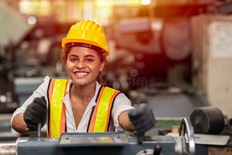 Jugendlich Arbeitnehmer des Mädchens mit lächelnder Schutzhelmglücklicher Arbeitsarbeit in der Industriefabrik mit Stahlmaschine