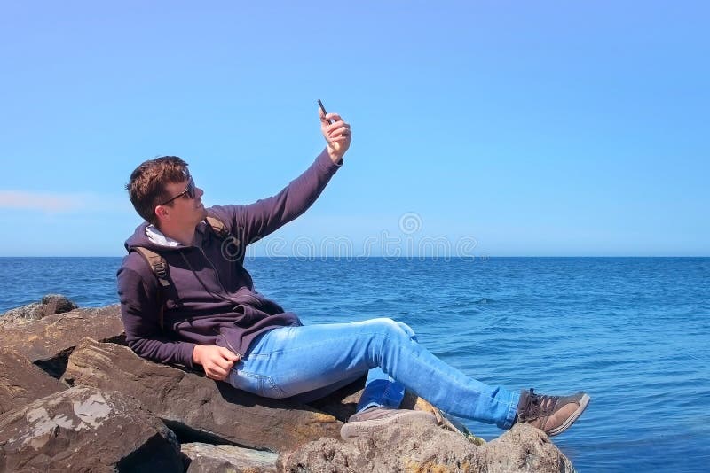 Jugendlicher TouristenreisebBlogger macht sich auf Smartphone auf Seeston auf Stein stockfotografie