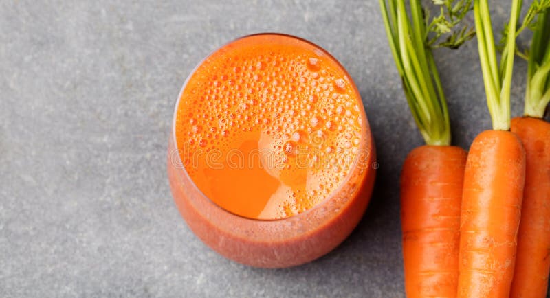 Jugo de zanahoria en comida sana de las zanahorias de cristal y frescas en una opinión superior del fondo de piedra gris imágenes de archivo libres de regalías Jugo de zanahoria en comida sana de las zanahorias de cristal y frescas en una opinión superior del fondo de piedra gris imágenes de archivo libres de regalías