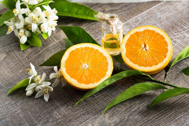 Juicy Orange cut in two parts and neroli, flowers of orange tree, on rustic wood background.