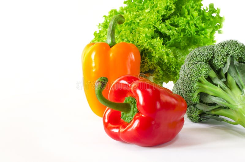 Juicy red and orange peppers with a green tail lies next to Bundle of lettuce and broccoli are on a white background