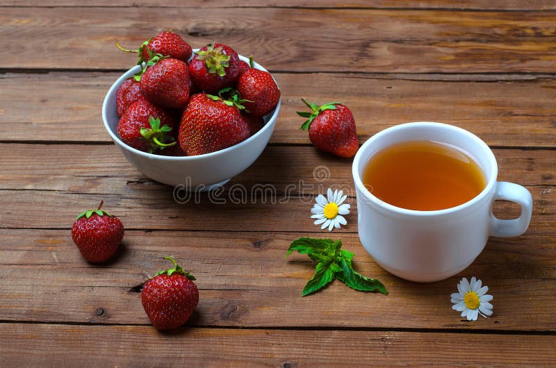 Juicy strawberries and a cup of tea on a wooden table.