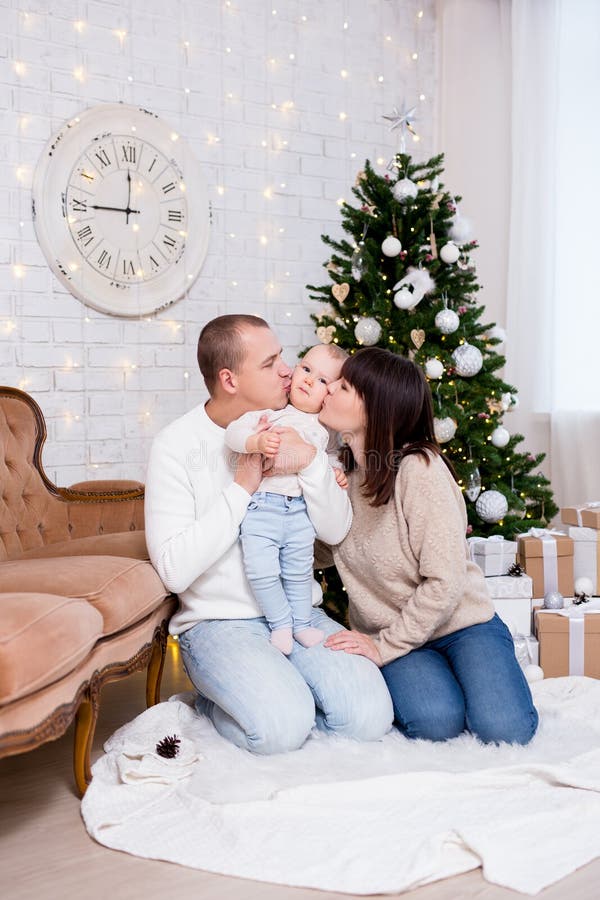 Jul- och familjebegreppet - lyckliga unga föräldrar kysser söt liten flicka dotter nära en dekorerad julgran arkivbilder Jul- och familjebegreppet - lyckliga unga föräldrar kysser söt liten flicka dotter nära en dekorerad julgran arkivbilder