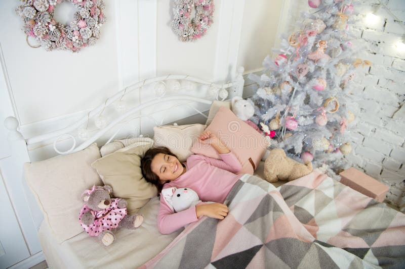 Julaftonbegrepp Väntande jul för barn i sovrum Ungen lägger, i att koppla av för säng Hemmet är det bästa stället i världen Liten unge för flicka som kopplar av på ljus inre för säng med julgarneringar