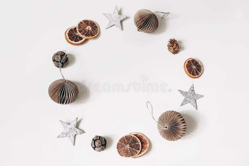 Christmas circle composition. Wreath of birch bark stars, larch cones and dry orange slices. Brown paper christmas ornaments, balls isolated on white table background, winter design. Flat lay, top. Christmas circle composition. Wreath of birch bark stars, larch cones and dry orange slices. Brown paper christmas ornaments, balls isolated on white table background, winter design. Flat lay, top.