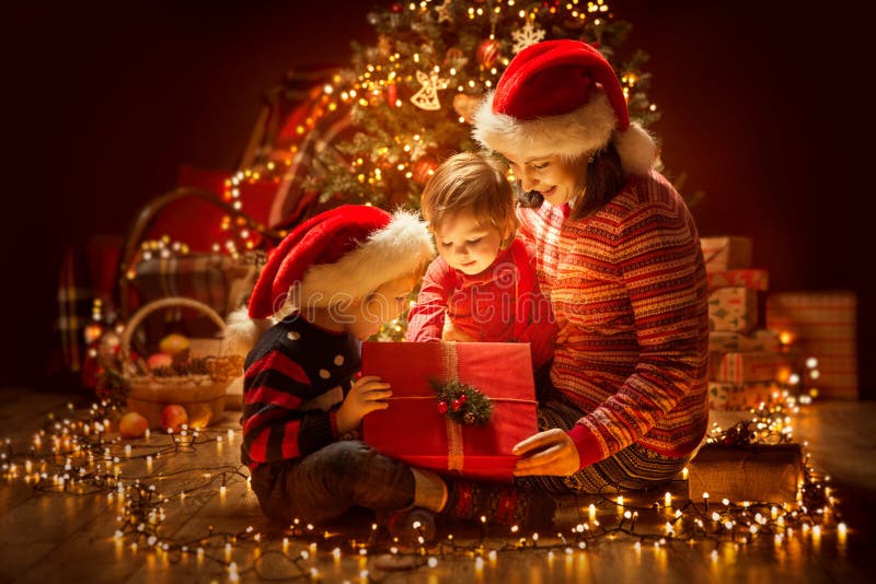 Julfamilj som öppnar tända den närvarande gåvaasken under Xmas-träd, lycklig moder och barn royaltyfri fotografi