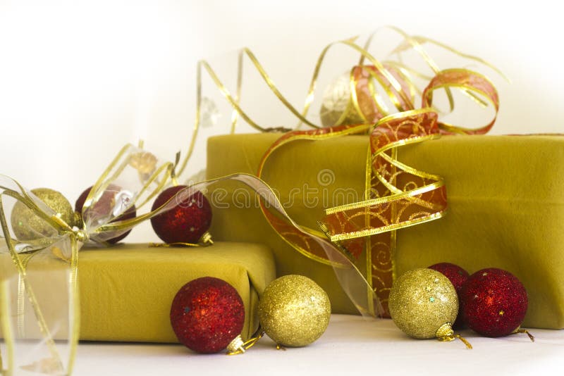 2 gifts wrapped with golden paper and red and golden ribbons. The gifts are surrounded by gold and red Christmas ornaments on a white background. 2 gifts wrapped with golden paper and red and golden ribbons. The gifts are surrounded by gold and red Christmas ornaments on a white background.