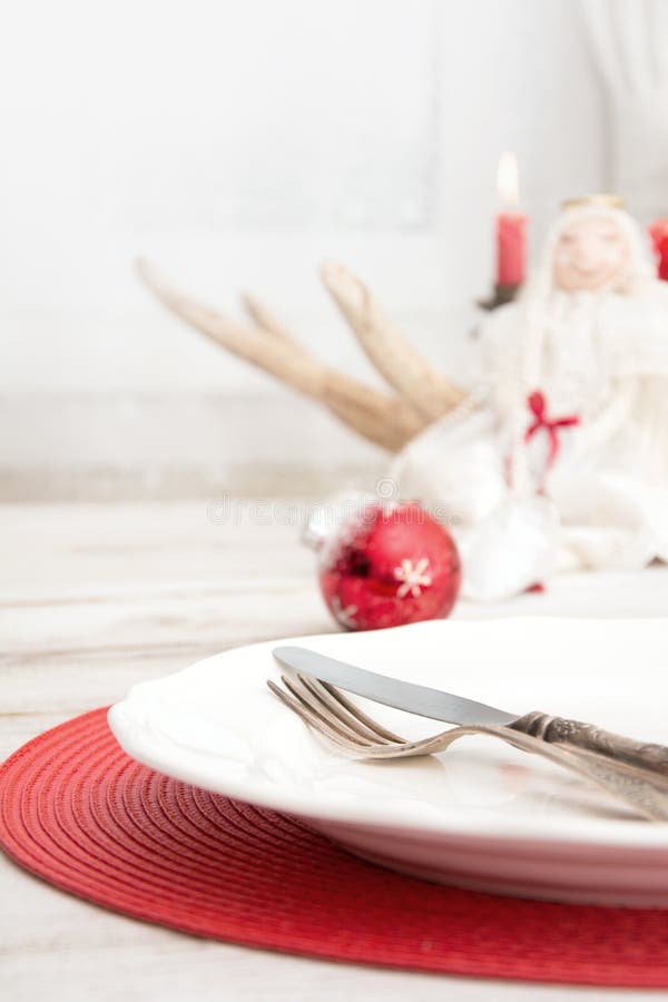 Julställeinställning med den vita dishwaren, bestick, bestick och röda garneringar på träbräde Jul