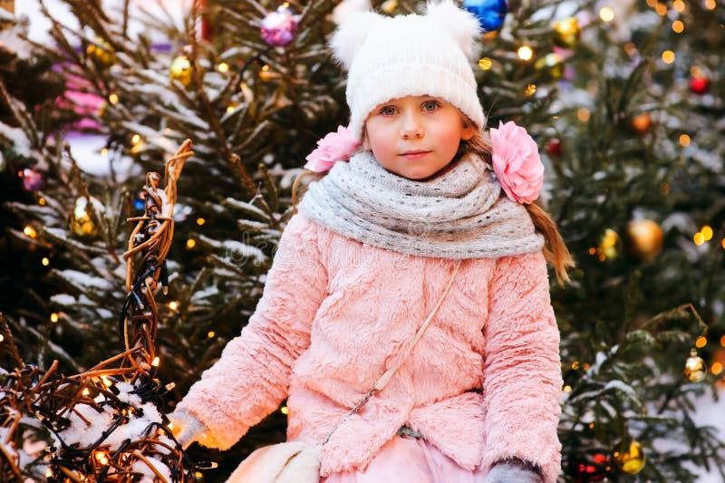 Julståenden av den lyckliga barnflickan som går utomhus- snöig vinter, dekorerade träd på bakgrund arkivbilder