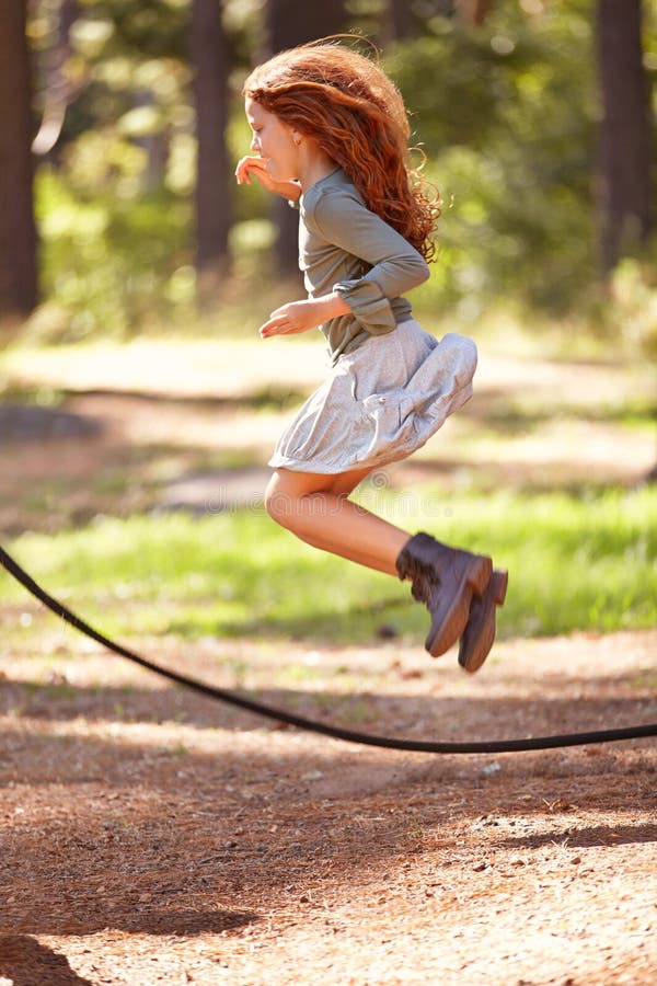 Jump, rope and girl outdoor for game in forest, park or playing on summer, holiday and vacation. Child, skipping and energy for fun activity in nature with trees in backyard or garden with kid in air.