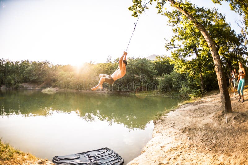 Jump into the water. A man is resting on the nature. A swing from a rope and a stick. Active recreation in nature. Friends have