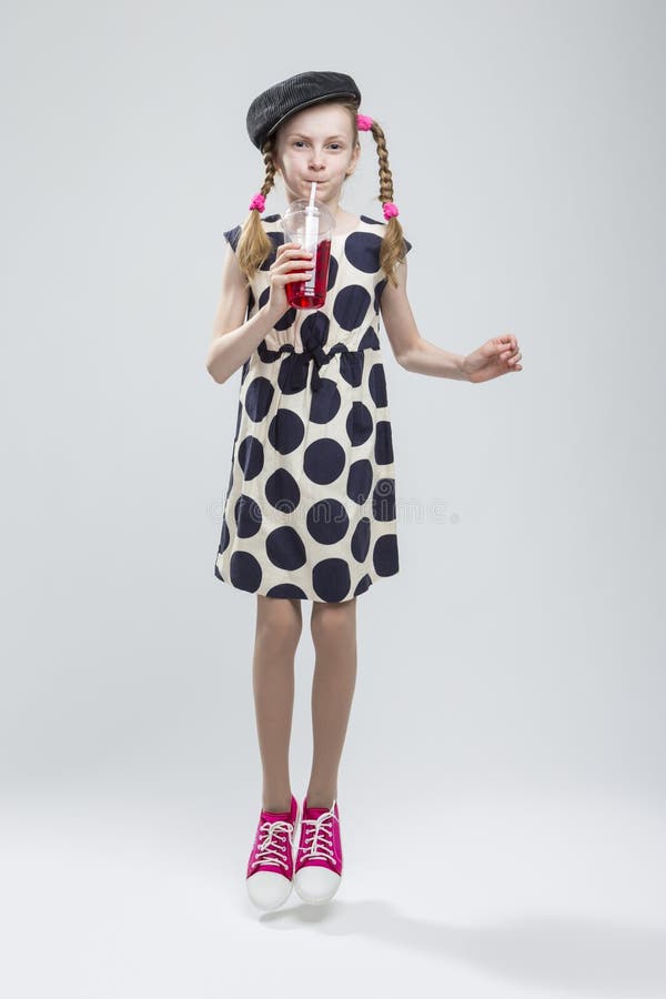 Jumping Caucasian Girl With Pigtails Posing in Gray Velvet Cap and Polka Dot Dress