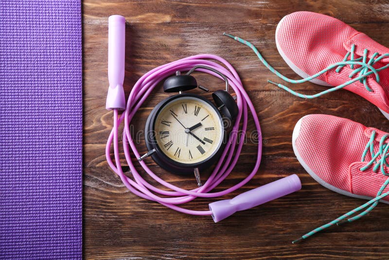 Jumping rope with alarm clock and sport shoes on wooden background royalty free stock photography Jumping rope with alarm clock and sport shoes on wooden background royalty free stock photography