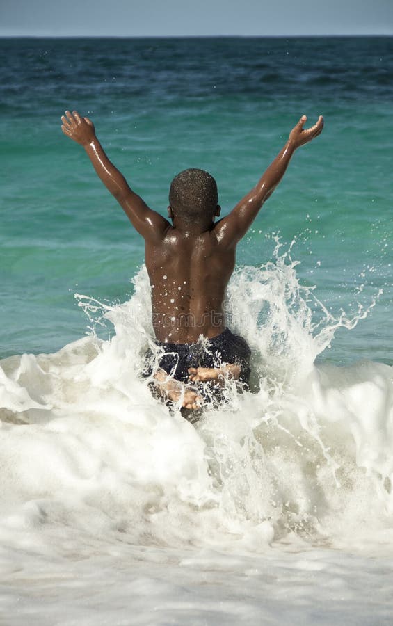 Bahamas ragazzo saltando tra le onde con le braccia in alto avendo un sacco di divertimento in spiaggia.