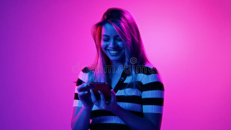 Jung lächelnde glückliche Frau mit Mobiltelefon für Kommunikation und soziale Medien vor rosa Studio Hintergrund in