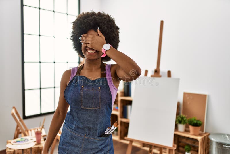 Young african american woman with afro hair at art studio smiling and laughing with hand on face covering eyes for surprise. blind concept. Young african american woman with afro hair at art studio smiling and laughing with hand on face covering eyes for surprise. blind concept