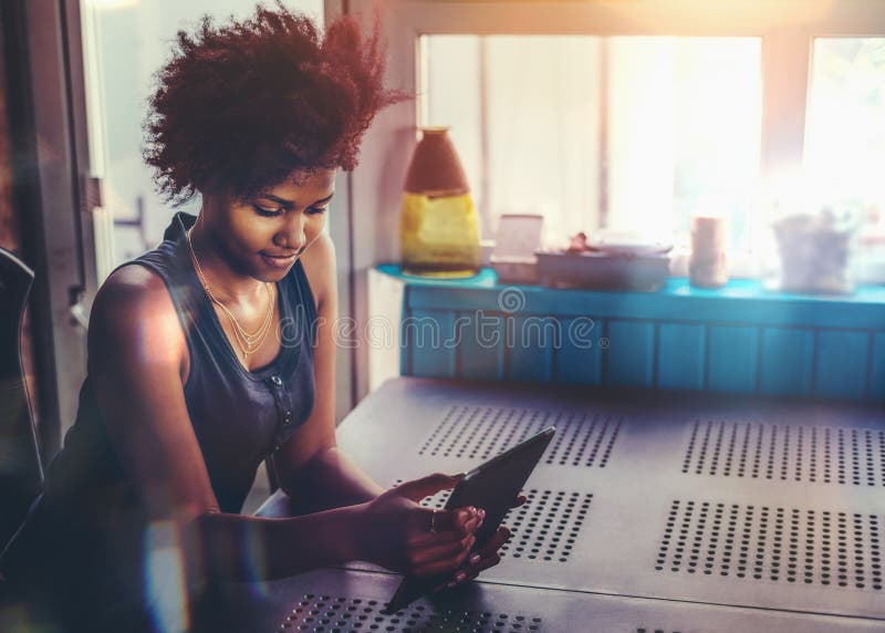 Junge Afrofrau am Tisch mit Tabletten-PC stockfotografie Junge Afrofrau am Tisch mit Tabletten-PC stockfotografie