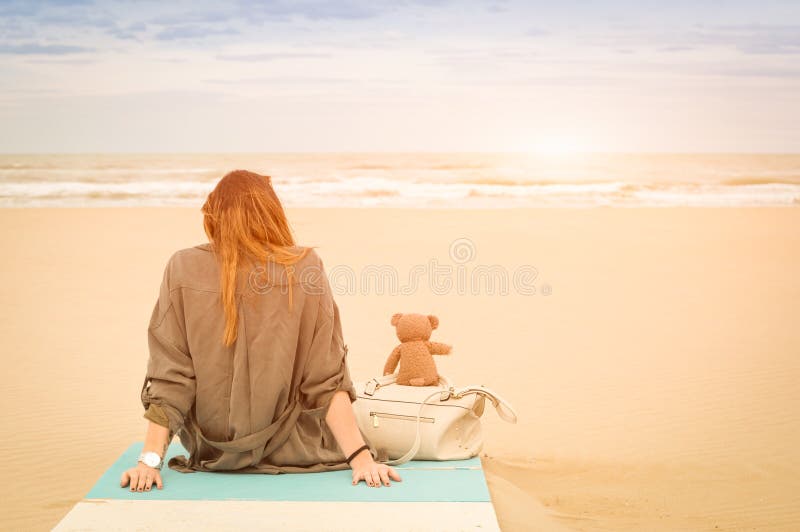 Junge allein stehende Frau, die am Strand mit Teddybären sitzt lizenzfreie stockbilder