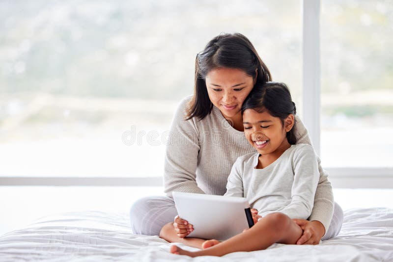 Junge, alleinerziehende Mutter, die eine digitale Tablette benutzt, während sie in einem bequemen Bett sitzt, mit sauberen weißen. Junge, alleinerziehende Mutter, die eine digitale Tablette benutzt, während sie in einem bequemen Bett sitzt, mit sauberem weißem Bett und sich mit ihrer Tochter entspannen kann. Mutter und ich morgens