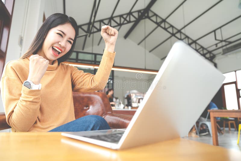 Junge attraktive asiatische Frau, welche die Laptop-Computer glaubt glücklichem nettem oder aufgeregtem Ausdruckerfolg oder -gewi lizenzfreie stockfotografie