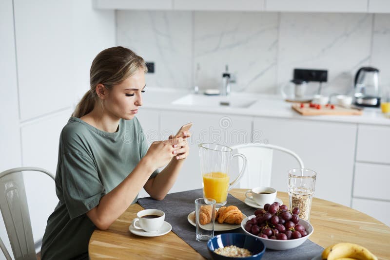 Junge attraktive Frau, die Smartphone beim Frühstücken verwendet lizenzfreie stockfotografie Junge attraktive Frau, die Smartphone beim Frühstücken verwendet lizenzfreie stockfotografie