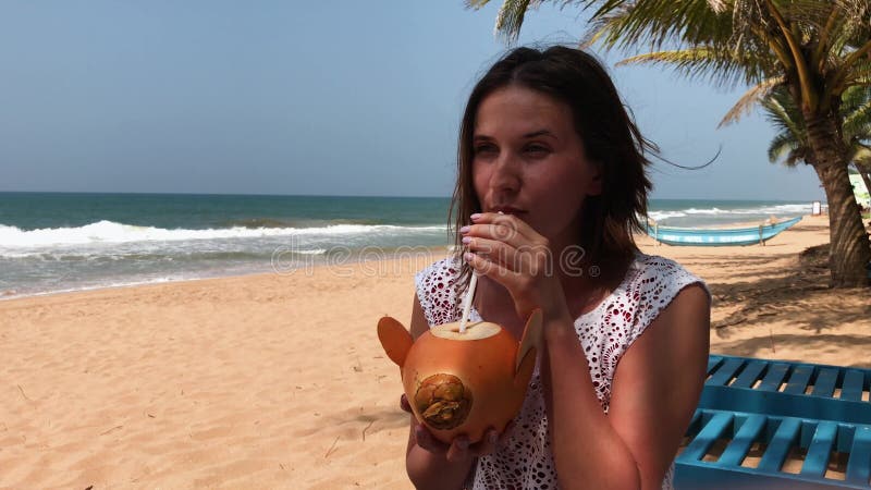 Junge attraktive sexy Frau im Urlaub, die durch Meer, tropischer Strand, trinkendes Cocktail in der Kokosnuss, herein reisend sit