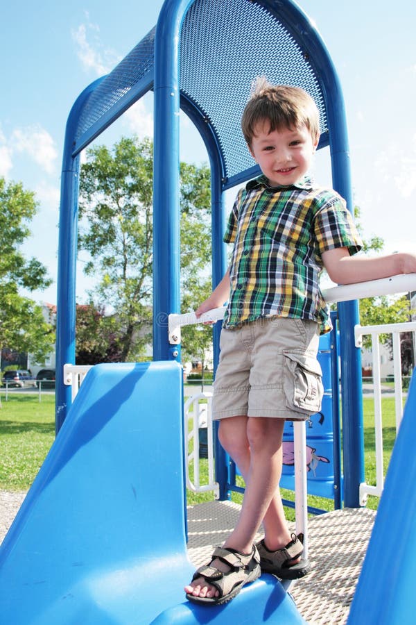 Smiling boy in summer attire, standing at the top of a playground sliding board. Smiling boy in summer attire, standing at the top of a playground sliding board.