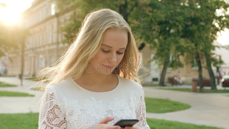 Junge blonde Dame Walking und unter Verwendung eines Telefons in der Stadt lizenzfreie stockbilder Junge blonde Dame Walking und unter Verwendung eines Telefons in der Stadt lizenzfreie stockbilder