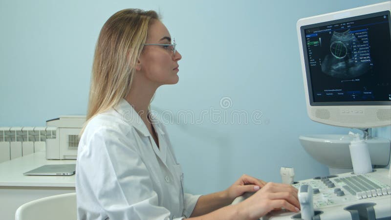Junge blonde Ärztin, die ein Ultraschallergebnis ansieht lizenzfreie stockbilder Junge blonde Ärztin, die ein Ultraschallergebnis ansieht lizenzfreie stockbilder