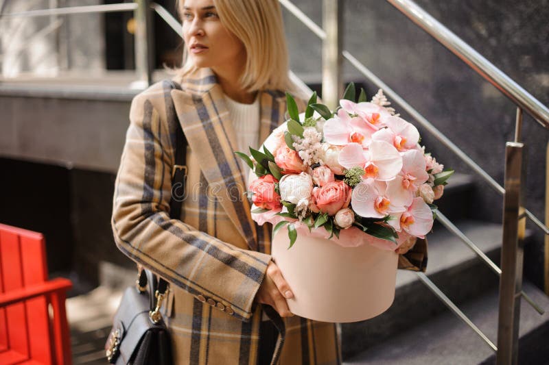 Junge Blondine halten Runden rosa Feld mit Blumengesteck von Pfingstrosen und Orchideen und sieht weg. lizenzfreie stockfotos