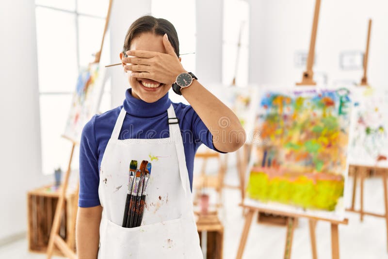 Young brunette woman at art studio smiling and laughing with hand on face covering eyes for surprise. blind concept. Young brunette woman at art studio smiling and laughing with hand on face covering eyes for surprise. blind concept