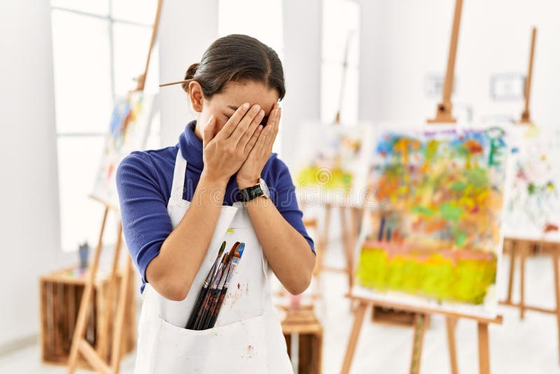 Young brunette woman at art studio with sad expression covering face with hands while crying. depression concept. Young brunette woman at art studio with sad expression covering face with hands while crying. depression concept