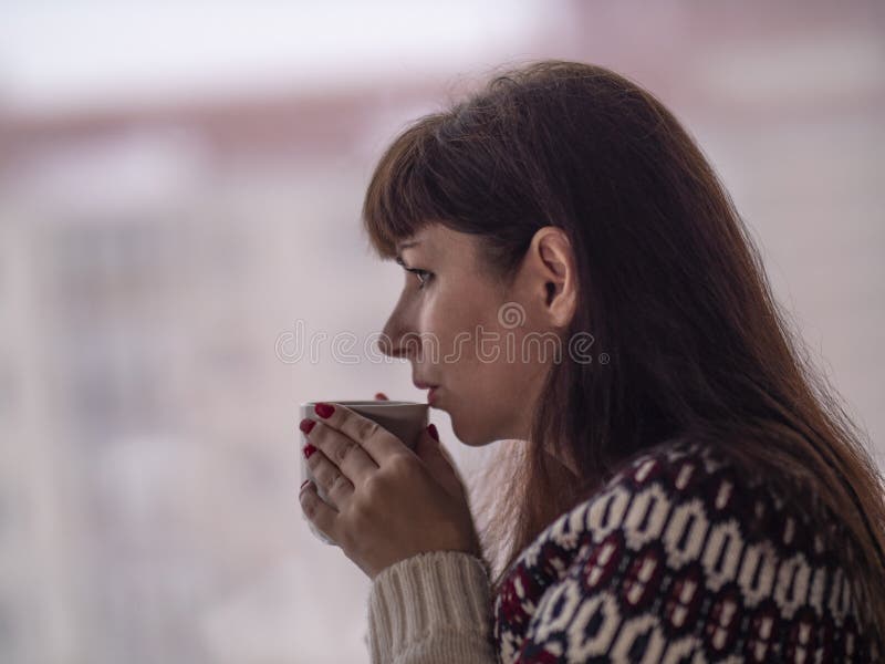 Junge brunette Frau trinkt Kaffee und schaut heraus das Fenster durchdacht stockfoto Junge brunette Frau trinkt Kaffee und schaut heraus das Fenster durchdacht stockfoto