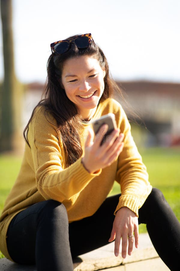 Junge chinesische Frau lächeln, die draußen mit dem Handy sitzt lizenzfreie stockfotos