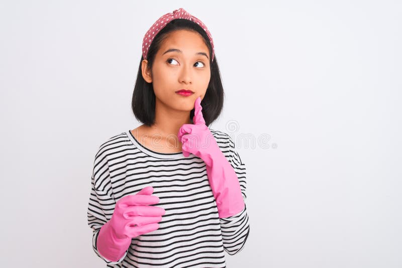 Junge chinesische Reinigerin, die sich mit Handschuhen über isolierten weißen Hintergrund reinigen, ernstes Gesicht, das über Frag. Junge chinesische Reinigerin mit Handschuhen über isolierten weißen Hintergrund ernsthaftes Gesicht denken über Frage sehr verwirrt Idee