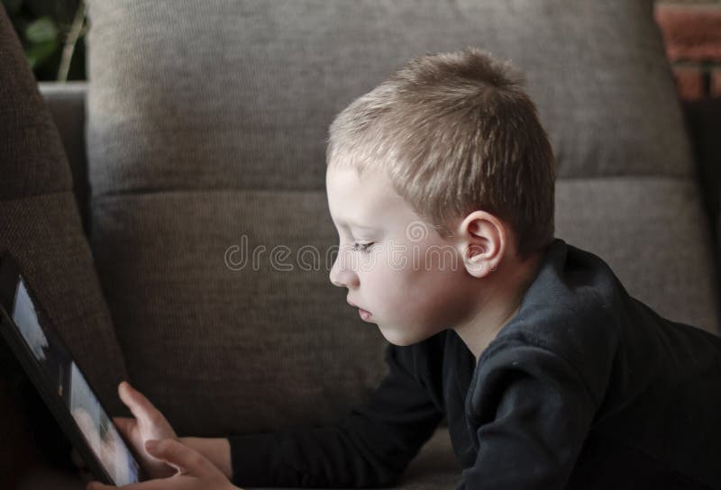Junge, der auf Sofa im Wohnzimmer und aufpassenden Karikaturen auf Tablette sitzt Porträt eines intelligenten Vorschule- Kindes u stockfotografie Junge, der auf Sofa im Wohnzimmer und aufpassenden Karikaturen auf Tablette sitzt Porträt eines intelligenten Vorschule- Kindes u stockfotografie