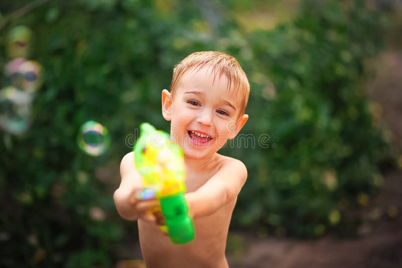 Junge, der mit Seifenblasen Nahaufnahme Kopienraum spielt. Der Junge im Sommer schießt eine Wasserpistole Kinderspiele mit Wasser lizenzfreie stockfotografie