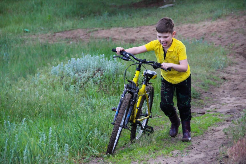 Junge in einem gelben T-Shirt rollt Fahrrad einen Berg und Lächeln.
