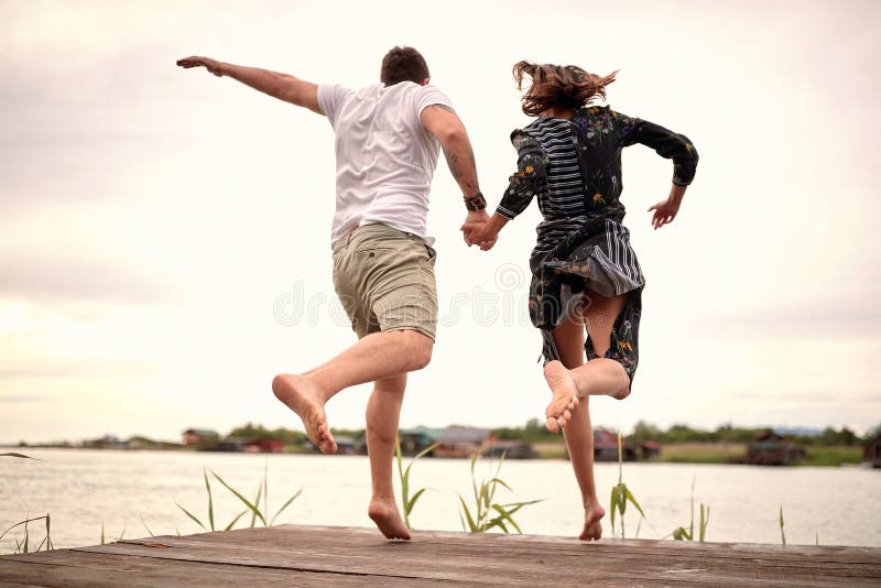 Junge erwachsene Paare, die zusammen in das Flusshändchenhalten springen.