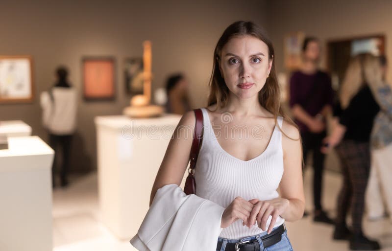Junge Frau auf der Ausstellung im Museum mit Besuchern im Hintergrund lizenzfreie stockfotos
