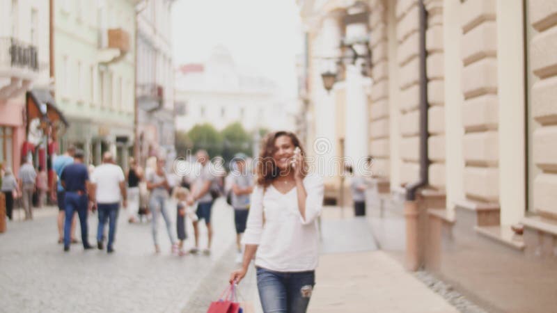 Junge Frau an der Straße mit Einkaufstaschen sprechend am Handy