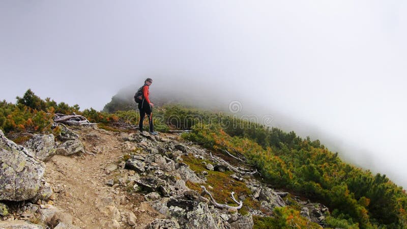 Junge Frau des Trekkings, die vom Berg mit einem Rucksack und Wanderstöcken überschreiten, wenn es darum geht,. Treck unter Wolken