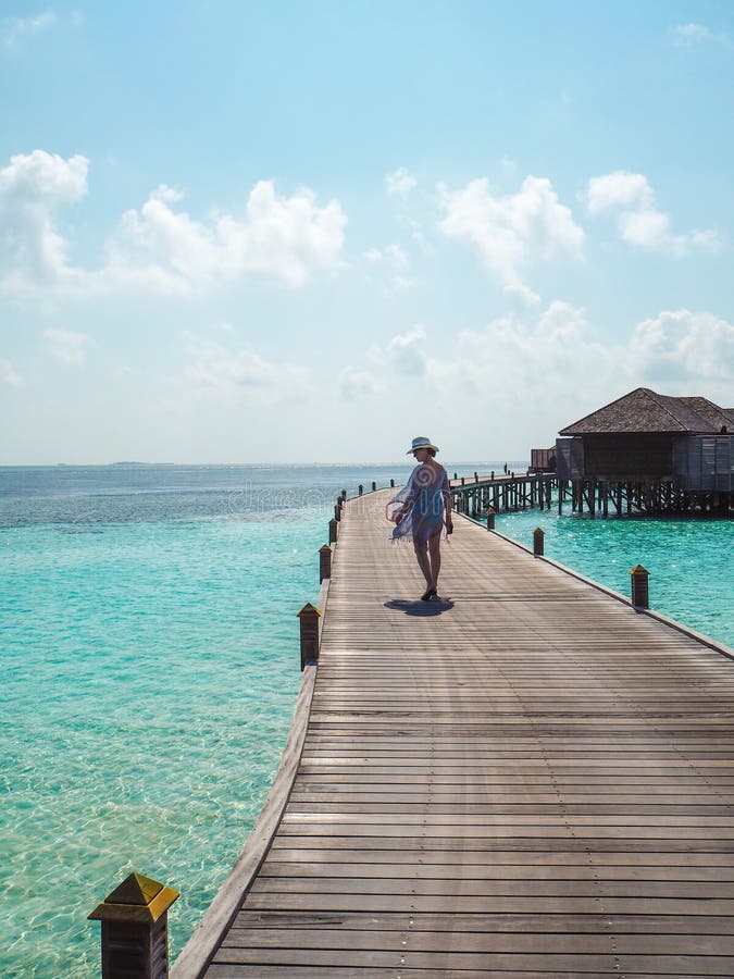 Junge Frau, die auf einen hölzernen Pier in den Malediven schlendert lizenzfreies stockbild Junge Frau, die auf einen hölzernen Pier in den Malediven schlendert lizenzfreies stockbild