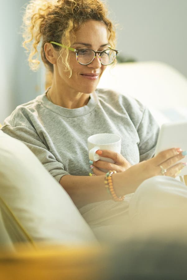 Junge Frau, die auf elektronischem Lesetablett ebook liest, sitzt bequem auf dem Sofa zu Hause in der Freizeit im Innenbereich. Me stockfotografie