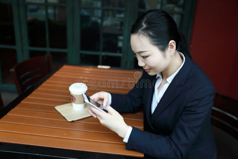 Junge Frau, die in der Kaffeestube am Holztisch, an trinkendem Kaffee sitzt und Smartphone verwendet Auf Tabelle ist Laptop lizenzfreie stockfotografie Junge Frau, die in der Kaffeestube am Holztisch, an trinkendem Kaffee sitzt und Smartphone verwendet Auf Tabelle ist Laptop lizenzfreie stockfotografie