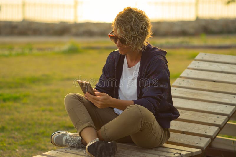 Junge Frau, die draußen mit Handy in ihren Händen sitzt stockfotos Junge Frau, die draußen mit Handy in ihren Händen sitzt stockfotos