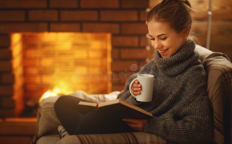 Junge Frau, die ein Buch durch den Kamin auf einem Winter evenin liest