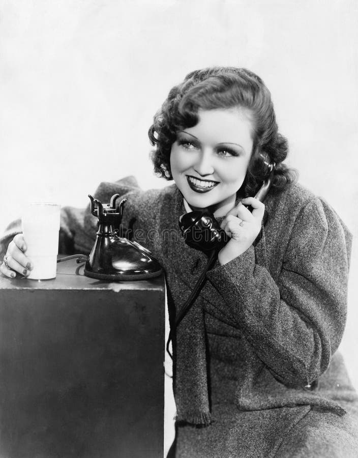 Young woman holding a glass of milk and talking on a rotary phone (All persons depicted are no longer living and no estate exists. Supplier grants that there will be no model release issues.). Young woman holding a glass of milk and talking on a rotary phone (All persons depicted are no longer living and no estate exists. Supplier grants that there will be no model release issues.)