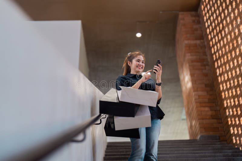 Junge Frau, die gerne mit mehreren Taschen einkaufen und Smartphone im modernen urbanen Umfeld benutzen lizenzfreie stockfotografie